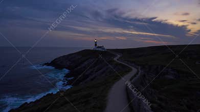 Coastal lighthouse transition from sunset to night with illuminated beacon