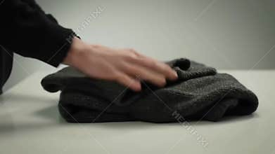 Person Carefully Folding a Dark Sweater on a White Table