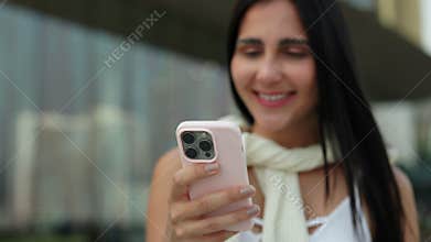 Portrait of cheerful Brazilian woman holds smartphone in pink case near store