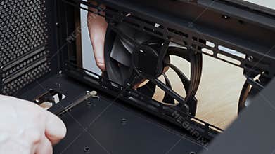 A computer technician unscrews a screw that secures a fan to a PC case. Assemble a computer system unit into a modern workstation