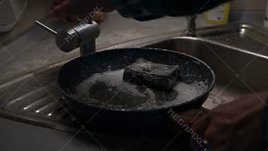 Man washing frying pan in kitchen sink