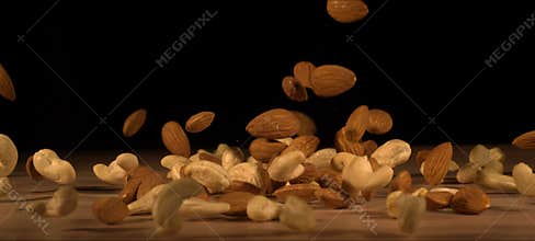 Super slow-motion of almonds and cashews fall on wooden table. Healthy snack, satisfying crunch.
