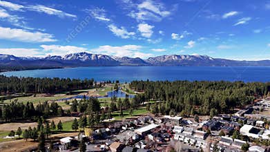 Aerial drone view of South Lake Tahoe golf course and town with blue lake and snowy mountain background