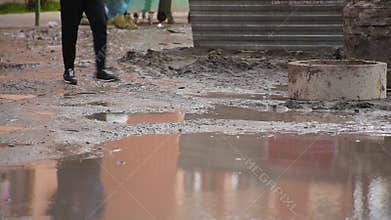 Close-up male legs going at residential yard through broken dirty road with huge puddle in which man is reflected
