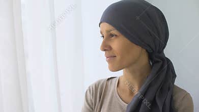 Happy woman in headscarf looking in window, recovery after cancer treatment