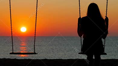 Silhouette of a girl swinging at sunset