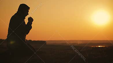 Silhouette young man praying outside at beautiful sunset. Male asks for help finding solace in faith, concept religion.
