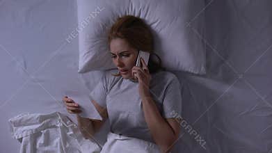 Woman trying to call to her man lying in bed and looking at photo, betrayal