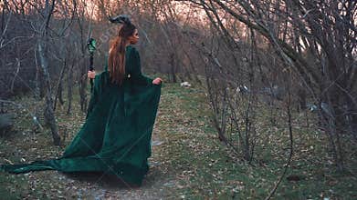 Ancient spirit of forest, lady in a long emerald velor dress with long flying sleeves and hem, evil nymph goes to punish