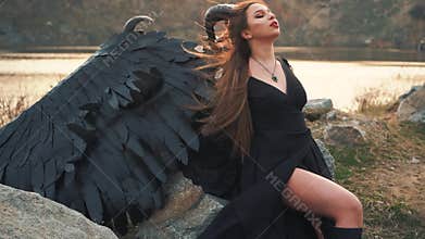 Terrible demonic messenger feeds on energy of sun, girl of Satan with big black strong wings and sharp horns on her head