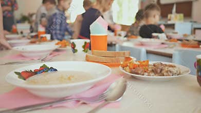Preparation for a lunch break in the kindergarten. Children sit down at the table with cooked food. The Russian