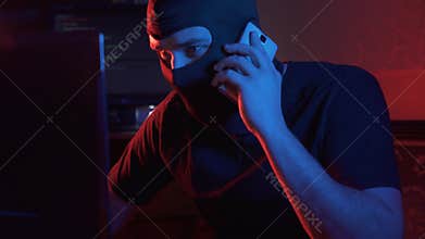 An anonymous man in a balaclava communicates by phone