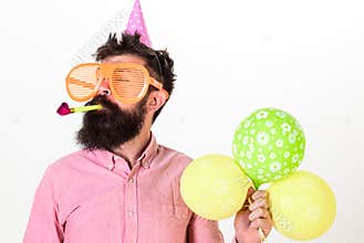 Man with beard and mustache on calm face holds air balloons, white background. Guy in party hat with party horn