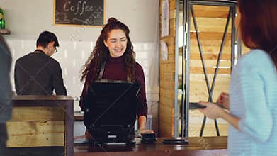 Attractive woman talkative cashier is accepting contactless payments with mobile phone and talking to customers and