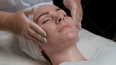 Carboxytherapy. The hands of the cosmetologist in the beauty salon begin to cleanse the face of a beautiful girl with closed eyes.