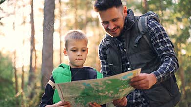 Slow motion of happy family father and cute son looking at map and talking during hike in forest in autumn. Trees