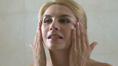 Woman dripping cosmetic oil on her face in bathroom, helpful healthy acids