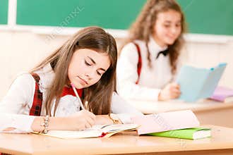 Schoolgirls in school uniforms sit for couples in the classroom. Girls go to school.