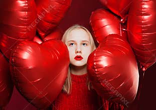 Young beautiful teen girl looking up on red heart balloons background