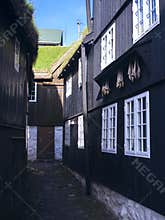 Black-tarred grass-roofed houses with dried fish hanging on hooks and narrow cobblestone street in Tórshavn.