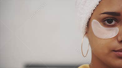 Closeup portrait of beautiful woman after bath with towel on head puts patches under the eyes from wrinkles and dark