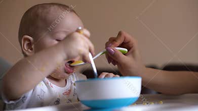 Mom feeds her cute little baby with a spoon