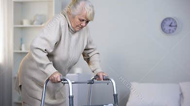 Old lady learning to walk with frame, rehabilitation after hip joint replacement