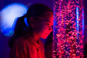 Child in therapy sensory stimulating room, snoezelen. Child interacting with colored lights bubble tube lamp during therapy.