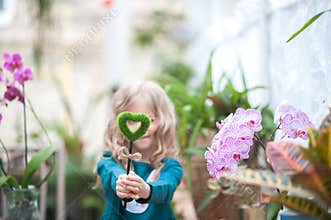 Girl in orchid greenhouse and love of nature and ecology. A girl with blooming orchids holding a heart and a cross