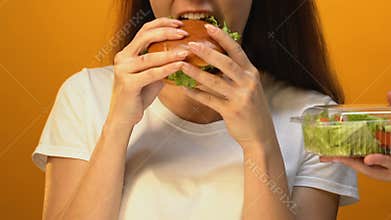 Hungry woman choosing fatty hamburger instead of green salad, risk of overweight