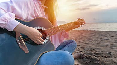 Woman`s hands playing acoustic guitar, capture chords by finger on sandy beach at sunset time. playing music concept