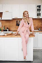 Gorgeous blonde woman in pink suit with loaf of bread on kitchen countrer.