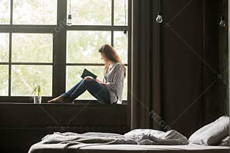Smiling woman enjoying new bestseller book sitting on window sil
