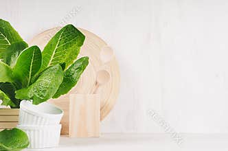 White modern kitchen decor with beige natural wooden dish, utensils, green plant on wood background.