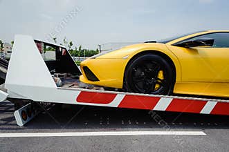 A broken vehicle strapped down to the platform of flat bed tow truck