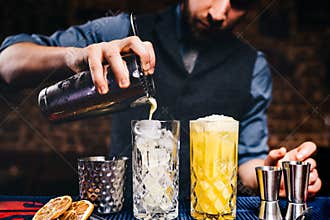 Vintage bartender pouring fresh orange vodka cocktail over ice in crystal glassware