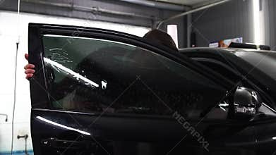 Master installs tint film for car glass with hairdryer and spatula with glare of light. Concept tinting