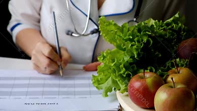 Nutritionist woman writing diet plan on table full of fruits and vegetables