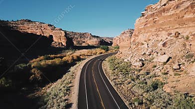 Camera following car driving away on highway road between big steep sunny canyon mountains covered with sand and rocks.