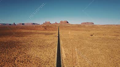 Drone flying backwards high above empty sandstone desert road in Monuments Valley, Arizona with flat mountains skyline.