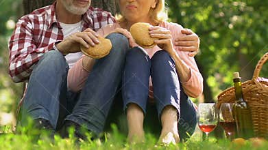 Old couple eating burgers outdoors, junk food increase cholesterol, healthcare