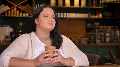Big dreamy caucasian woman thinking and holding her beverage in cafe