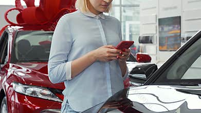 Woman using her smart phone at the car dealership salon