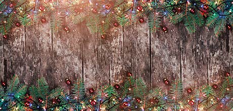 Christmas Fir branches with lights and red decorations on wooden background. Xmas and Happy New Year frame.