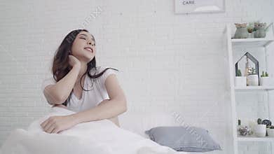 Happy beautiful Asian woman wake up, smiling and stretching her arms in her bed in the bedroom.