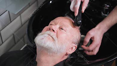 self-care, an elderly man in a barber chair wash his hair for cutting and styling in a barbershop