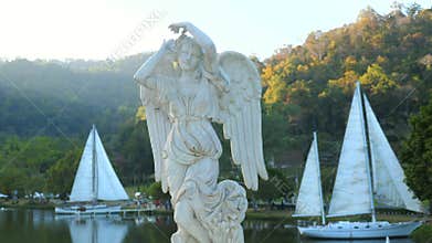 Antique stone female statue in sunset sunlight with yacht sail boats on background. Ancient sculpture of angel in public