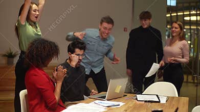 Group of cheerful young business people having meeting using laptop excited raise hand up celebrating to success