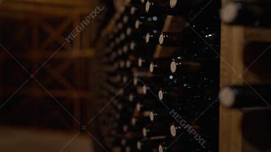 Live camera moves along rows of corked wine bottles stacked in wine cellar indoors. Expensive high-quality beverage in