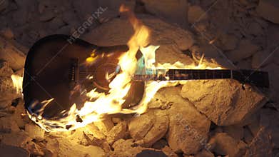 Guitar burning is on fire on stones. Acoustic western guitar burn in darkness. Flame envelopes the guitar